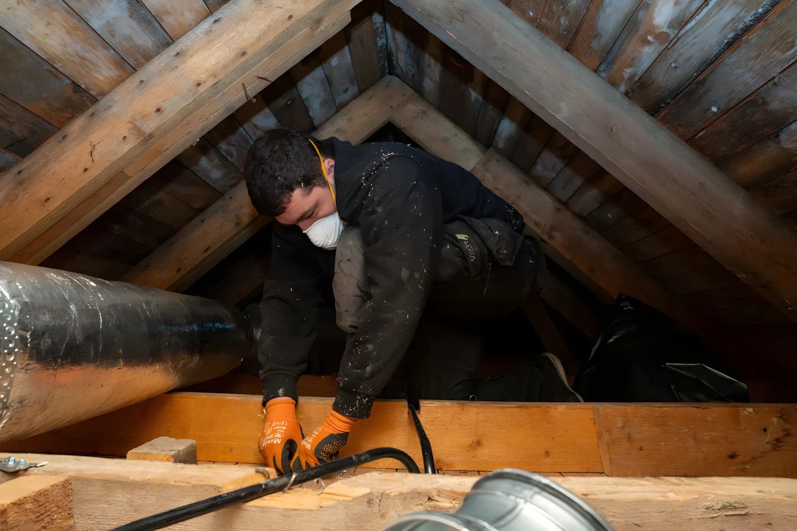 Vår tekniker fäster ventilationskanaler vid bjälklaget på en vind hos en kund i Stockholm