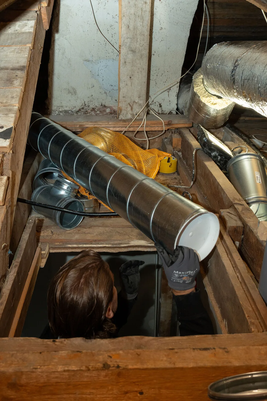 Två tekniker från Aerius drar nya ventilationskanaler genom en lucka på en gammal vind vid ett byte från självdrag till mekanisk ventilation