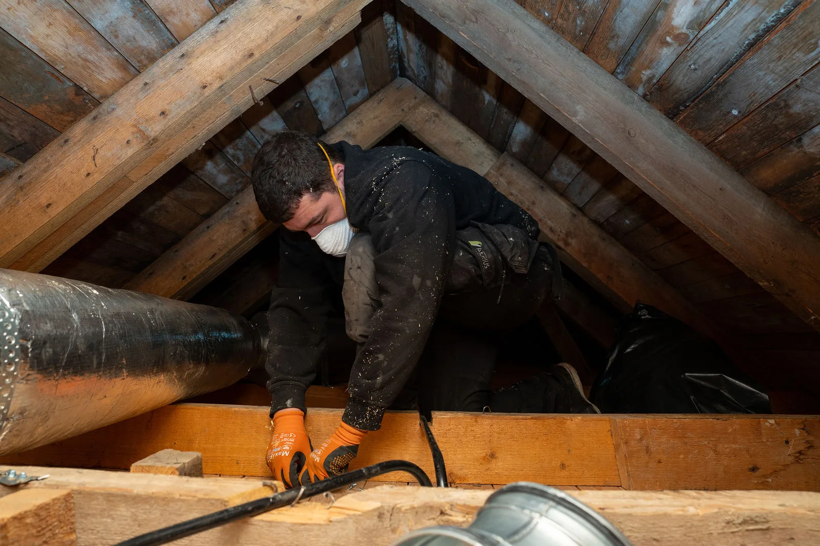 Montör kryper mellan takstolarna på en trång vind under FTX-installation i Osby