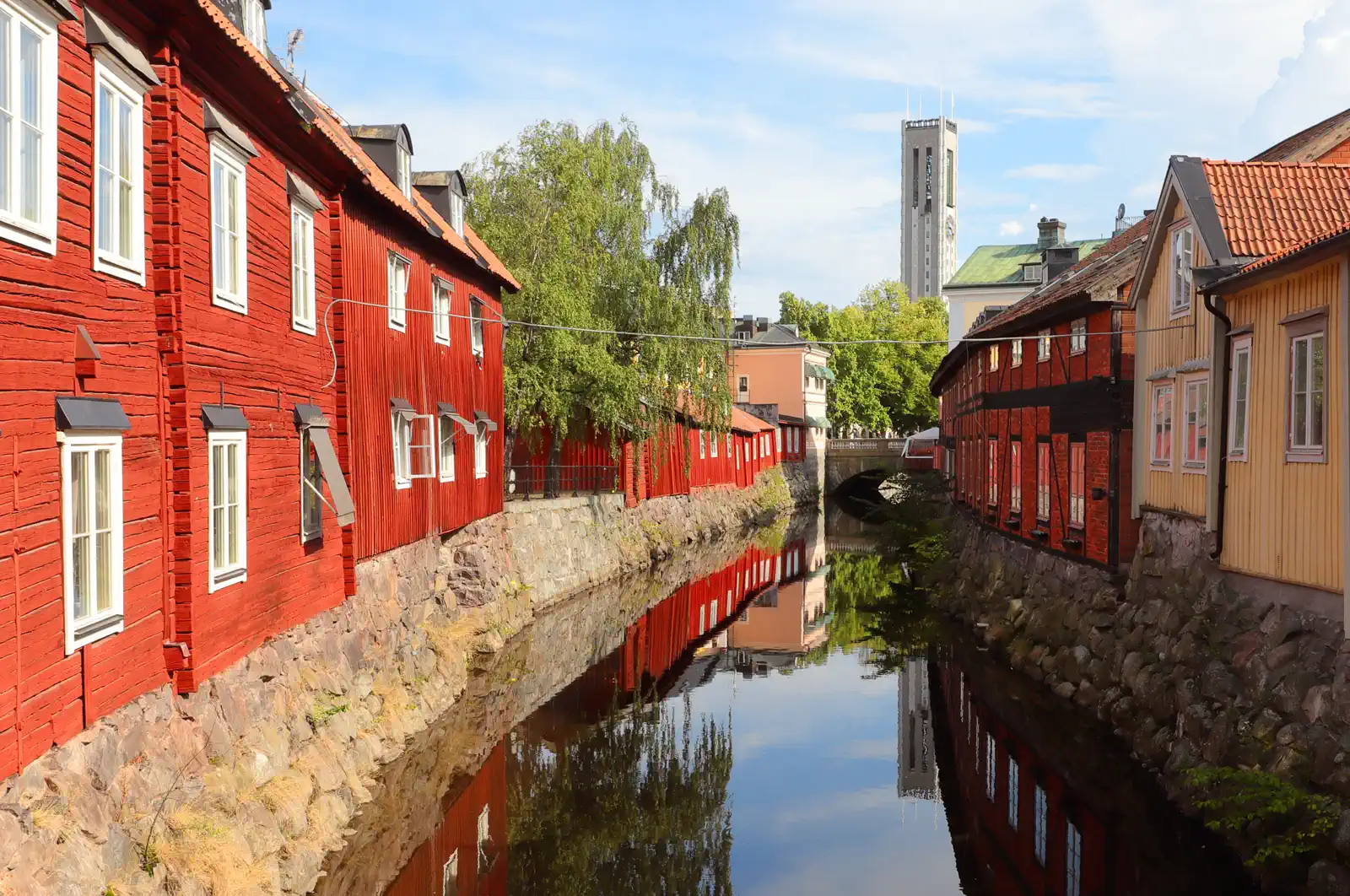 Röda trähus längs Svartån i Västerås med Stadshustornet i bakgrunden, mitt i staden där vi hjälper husägare med ventilation